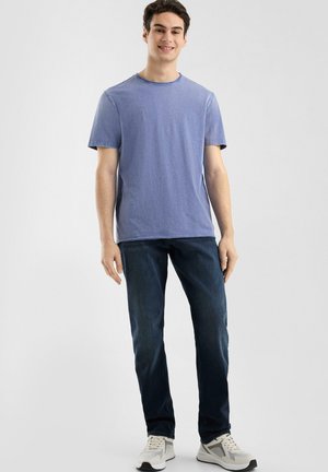 Camiseta de algodón azul claro con mangas cortas, cuello redondo y una textura sutil, combinada con jeans oscuros y zapatillas deportivas blancas.