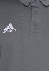 Grå polo shirt lavet af glat stof, med tre knapper og en klassisk krave. Adidas-logo broderet i hvidt på venstre bryst.