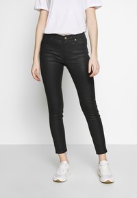 Svarta denim skinny jeans med medelhög midja, fem fickor och en slät yta, i kombination med vita sneakers.