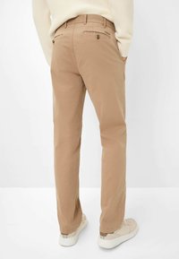 Persona che indossa chinos beige con tasche posteriori con bottone e un maglione color crema, in piedi con le mani nelle tasche e scarpe da ginnastica bianche.