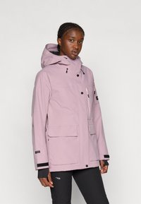 Világos rózsaszín vízálló dzseki kapucnival, cipzárral és patentos záródással, elülső zsebekkel, valamint fekete díszítéssel a mandzsettákon és a zsebeken. Sima textúra.