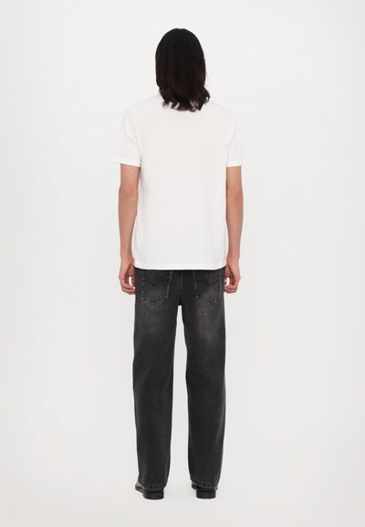 Hvid bomulds T-shirt med korte ærmer, parret med løstsiddende mørkegrå jeans med stikninger på baglommen. Flade sko.
