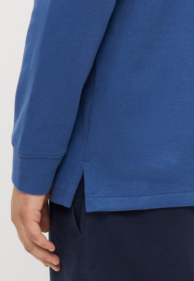 Blue long-sleeve shirt made of textured fabric with side slits at the hem. Features a round neck and ribbed cuffs.
