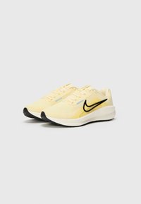 Svetlo rumene atletske čevlje z zračno mrežasto zgornjim delom, črnimi Nike logotipi in kontrastnimi modrimi detajli na vezalkah. �Črna gumijasta podloga.