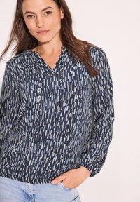 Blusa a righe navy con strisce verticali in azzurro chiaro e bianco, dotata di scollo a V, maniche lunghe e polsini arricciati.
