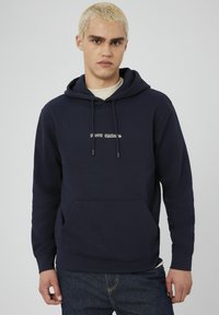 Hoodie bleu marine en tissu doux, avec une poche kangourou sur le devant et un texte brodé blanc dans une police décontractée sur la poitrine.