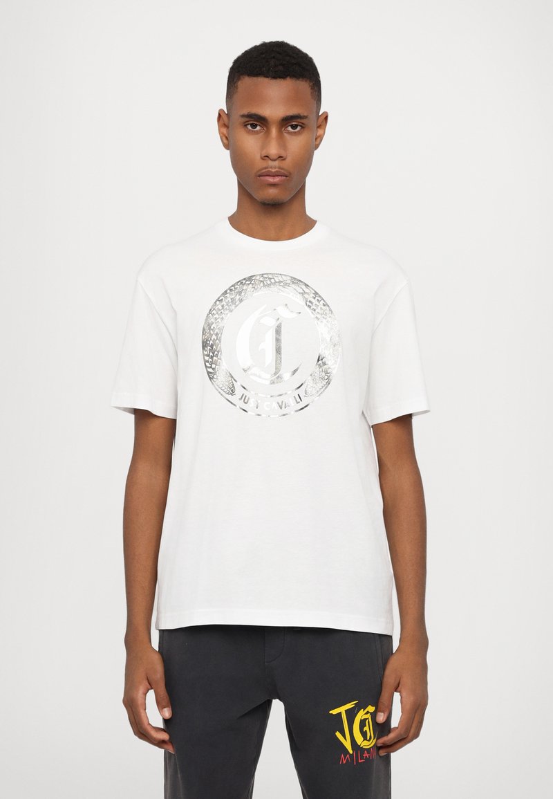 Hvid kortærmet t-shirt med et metalisk logo-design i midten. Blødt stof, afslappet pasform, rund halsudskæring, ingen synlige mønstre eller accenter.