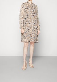 Blommönstrad beige klänning med långa ärmar, samlad halsringning och en lös silhuett. Matchad med beige plattformssandaler.