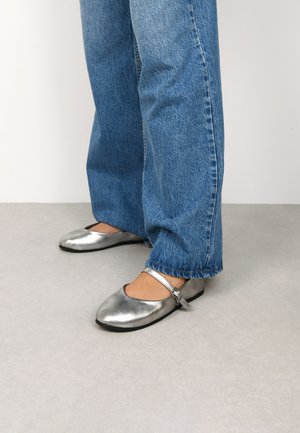 Ballerine metalliche argentate con punta arrotondata e una sottile cinghia alla caviglia, abbinate a jeans in denim blu.