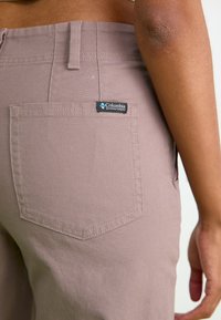 Columbia merkbroek in een licht mauve stof. Beschikt over een achterzak met een label, een gestructureerd oppervlak en zichtbare stiksel details.