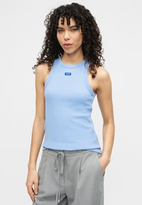 Ανοιχτό μπλε αμάνικο τοπ με ανάγλυφη υφή και στρογγυλή λαιμόκοψη. Διαθέτει μικρή μπλε ετικέτα με λογότυπο στο κέντρο. Φοριέται με γκρι παντελόνια.