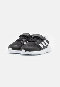 Baskets de sport noires avec tissu en maille et accents en cuir. Présentent des rayures blanches sur les côtés et une sangle Velcro pour la fermeture.