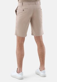 Beige Shorts mit flachem Bund, zwei Gesäßtaschen und glatter Textur. Kombiniert mit weißen Sneakers.