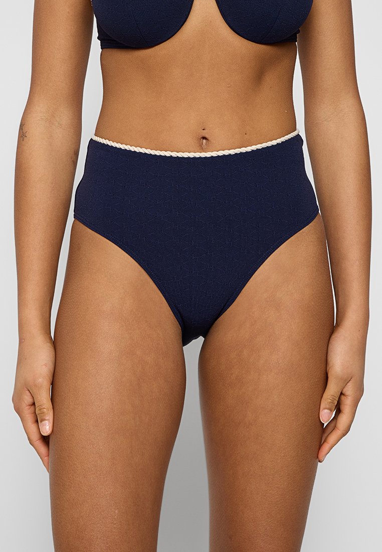 Hoch taillierter Bikini-Unterteil in dunkelblau mit strukturiertem Stoff und cremefarbenem geflochtenem Besatz an der Taille. Glatte Oberfläche und Design mit voller Abdeckung.
