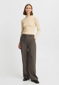 Beige gestreifter Rollkragenpullover kombiniert mit hoch taillierten, weit geschnittenen braunen Hosen. Glatter Stoff mit subtiler Textur; maßgeschneiderte Passform, klare Linien.