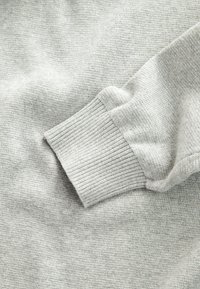 Lysegråt strikket stof med close-up af en ribbet kant på en langærmet sweater eller skjorte.