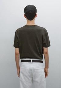Czarny bawełniany T-shirt w ciemnozielonym kolorze z okrągłym dekoltem, krótkim rękawem i luźnym krojem, zestawiony z białymi spodniami i czarnym paskiem.