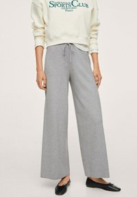 Pantaloni tuta grigi ampi in tessuto morbido, con elastico in vita e coulisse regolabile. Abbinati a una felpa color crema.