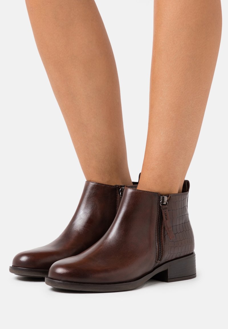 Bottines en cuir marron avec une finition lisse et un côté embossé façon croco, dotées d'un petit talon bloc et d'une fermeture éclair latérale.