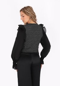 Bluză neagră cu mâneci lungi transparente și accente volan, având un material texturat, lucios de culoare gri la torace și o siluetă ajustată.