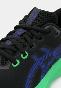 Chaussure de sport noire avec œillets verts, une tige en mesh texturé et des accents bleus sur les côtés. Comprend des lacets et un col rembourré pour le soutien.