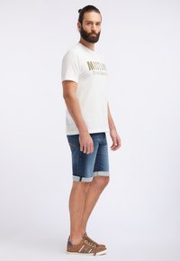 Balta trumpa rankovėmis marškinėliai su užrašu "True Denim", derinami su mėlynomis džinsinėmis šortais, pasuktais kraštais, ir rudos spalvos bateliais su raišteliais.