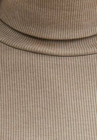 Beige geribbelde stof met een coltrui-ontwerp. De textuur heeft verticale strepen en een zachte, rekbare stof. Glad oppervlak met een subtiele glans.
