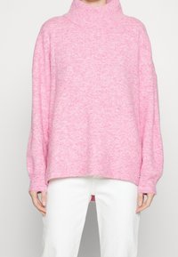 Pull col roulé rose oversize en tissu doux, avec poignets et ourlet côtelés, silhouette ample et légère texture.