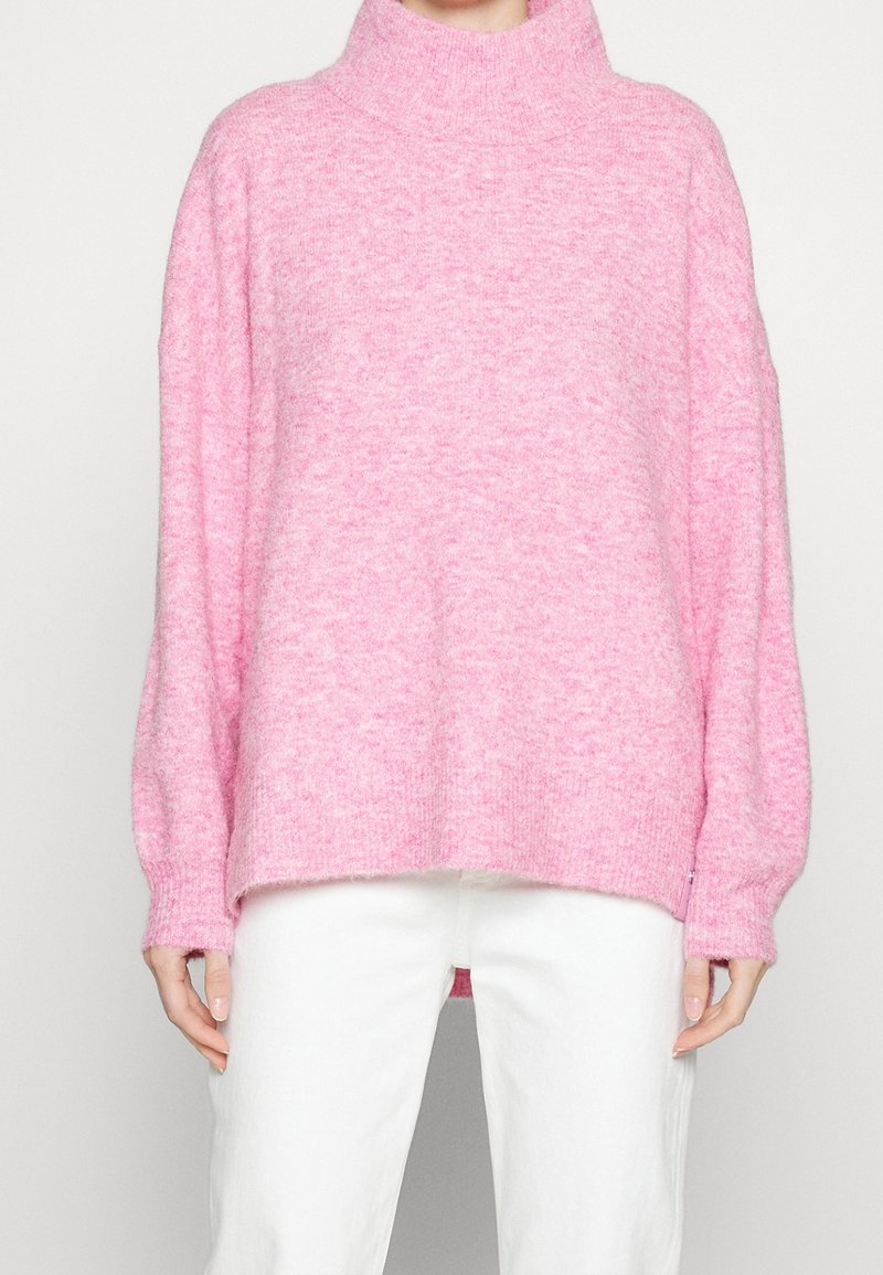 Pull col roulé rose oversize en tissu doux, avec poignets et ourlet côtelés, silhouette ample et légère texture.