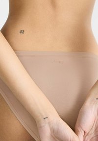 Beige nahtlose Unterwäsche mit glatter Textur und breitem Bund, mit dezent auf der Vorderseite aufgedrucktem "sloggi"-Logo.