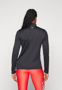 Haut sportif noir à manches longues avec un col montant et un logo au dos, associé à un legging rouge ajusté. Texture lisse et design près du corps.