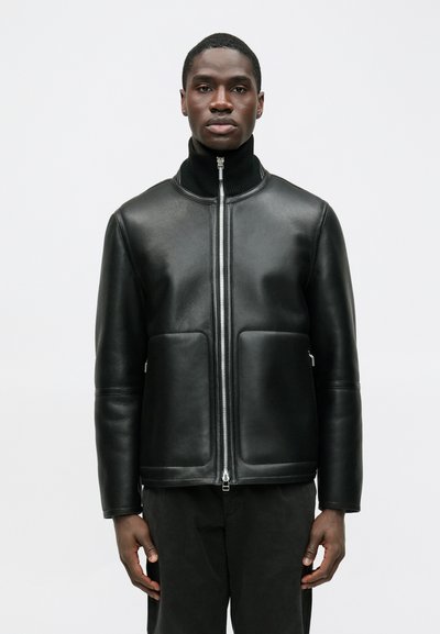 Schwarze Lederjacke mit hohem Kragen, Frontreißverschluss und zwei großen Vorder Taschen. Glatte Textur und minimalistisches Design.