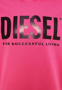 Rosa bomullströja med stor svart tryckt text "DIESEL" och mindre text "FOR SUCCESSFUL LIVING" nedanför, mjuk textur.