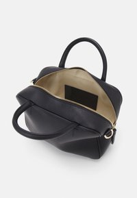 Sac à main en cuir noir avec deux poignées, fermeture éclair dorée partiellement ouverte pour montrer l'intérieur en tissu beige et une étiquette noire à l'intérieur.
