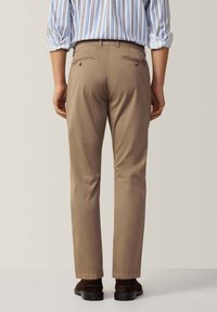 Chino beige con vestibilità slim, texture liscia, vita media, due tasche posteriori con bottoni e orlo con risvolto.