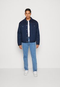 Chaqueta acolchada navy con botones a presión, dos bolsillos en el pecho y un cuello suave, combinada con jeans azul claro y zapatillas blancas.