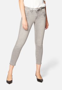 Jeans ajustados de mezclilla gris con cintura alta y puños enrollados. Presentan un sutil adorno de gemas en el bolsillo delantero. Textura suave.
