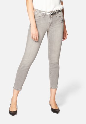 Jeans skinny en denim gris avec taille haute et ourlets retroussés. Présente un embellissement subtil en pierres précieuses sur la poche avant. Texture lissée.