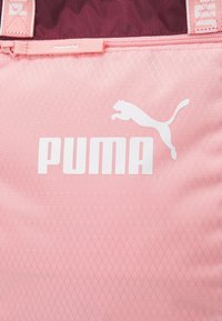 Bolsa de tela rosa con un patrón de diamante texturizado. Presenta un destacado logo blanco de Puma y una sección superior de color burdeos en contraste. Cierre de cremallera.