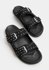 Czarne klapki na płaskiej podeszwie z dwoma regulowanymi paskami z srebrnymi klamrami, ozdobione dekoracyjnymi srebrnymi ćwiekami na miękkim materiale przypominającym zamsz.
