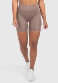 Shorts in spandex marroni a vita alta con una texture liscia e orlo doppio cucito, indossati con sneakers bianche su uno sfondo neutro.