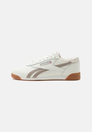 Hvid lavtop sneaker med lysegrå stribe accenter, gummisål og Reebok-logo med UK-flag på siden, vist mod en ensfarvet baggrund.
