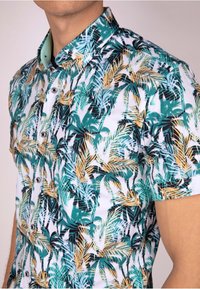 Chemise à manches courtes avec un motif de feuilles tropicales en bleu sarcelle, noir et or sur un fond blanc ; fermeture à boutons, col classique.