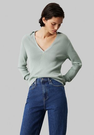 Lys grøn ribbet sweater med V-hals og lange ærmer, sammen med høj talje mørkeblå denim jeans.