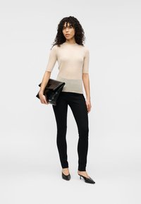 Μπεζ ριμπ πλεκτό τοπ με κοντά μανίκια, μαύρο εφαρμοστό παντελόνι, μαύρα ψηλοτάκουνα παπούτσια, κρατώντας γυαλιστερό μαύρο φάκελο. Ομαλή υφή, απλός σχεδιασμός.