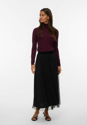 Woman wearing a burgundy turtleneck sweater, black sheer long skirt, and black open-toe heels, standing and looking to the side.