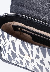 Borsa in pelle bianca e nera con design a strisce zebrate, dettagli in oro e una tasca interna con zip foderata in beige.