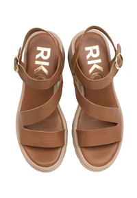 Brązowe skórzane sandały z krzyżującymi się paskami, zapięciem na kostkę i beżową podeszwą. Charakteryzują się gładką teksturą i złotym logo w środku.