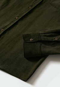 Chemise en velours côtelé vert foncé à manches longues avec poignets boutonnés et boutons sur le devant, posée à plat sur une surface claire.