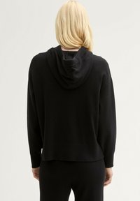 Felpa nera a maglia con cappuccio, realizzata in un materiale morbido, con maniche lunghe e una vestibilità rilassata. Tessuto testurizzato con un motivo sottile.
